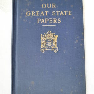 May include: A vintage book titled "Our Great State Papers" with gold lettering and a gold emblem on a blue cover. The book has a slightly worn appearance, suggesting age and use. The cover is a solid blue color.