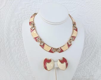 Puede incluir: Un conjunto de joyas vintage con un collar y pendientes a juego. El collar y los pendientes tienen una base de metal dorado con detalles de esmalte crema y burdeos. El collar se exhibe sobre un busto blanco.