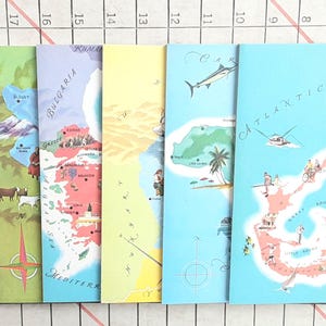 May include: A collection of vintage-style travel journals with illustrated maps. The journals feature colorful designs, including maps of Bulgaria, the Mediterranean Sea, and the Atlantic Ocean. Each journal has a unique color scheme and illustrations.