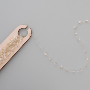 May include: A wooden tool with a loop for winding a strand of white and gold garland. The garland is also shown in a separate loop.
