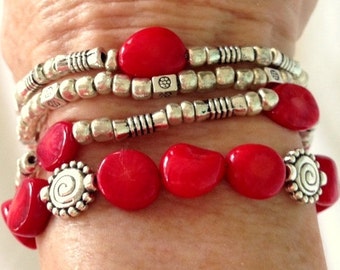 May include: A stack of bracelets with red coral beads and silver beads. The bracelets have a silver charm with a swirl design.