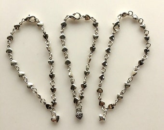 May include: Three silver heart charm bracelets with different charms. The first bracelet has a small heart charm, the second has a heart-shaped lock charm, and the third has a small heart charm.