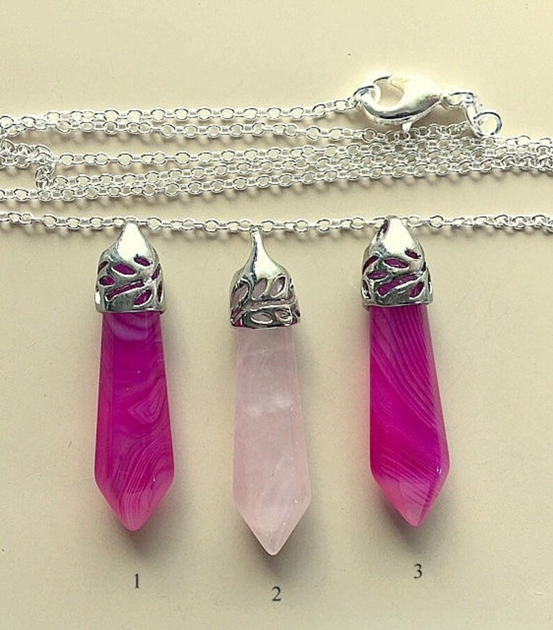 May include: Three silver pendant necklaces with different colored gemstone drops. The first pendant is a pink and white agate, the second is a light pink rose quartz, and the third is a pink and white agate. The pendants are numbered 1, 2, and 3.