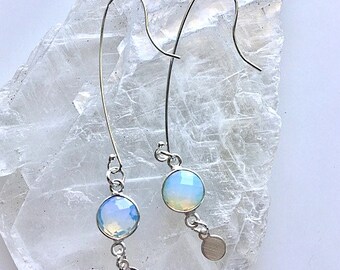 May include: A pair of silver dangle earrings with iridescent opal stones and silver discs hanging from the bottom.