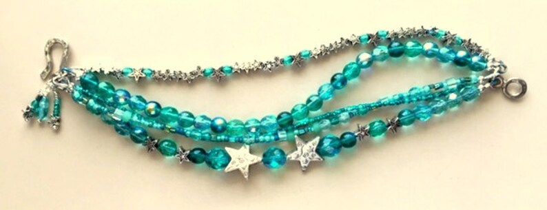 May include: Multi-strand bracelet with turquoise blue beads and silver star charms.
