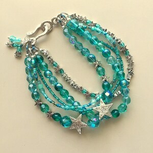 May include: Multi-strand bracelet with turquoise blue glass beads and silver star charms. The bracelet has a silver clasp.