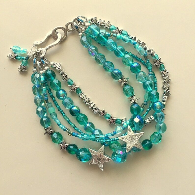May include: Multi-strand bracelet with turquoise blue glass beads and silver star charms. The bracelet has a silver clasp.