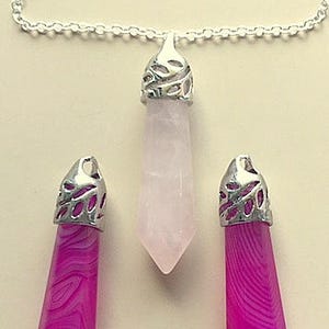 May include: Three crystal pendants on silver chains. The pendants are in the shape of a teardrop and are made of pink and white quartz.