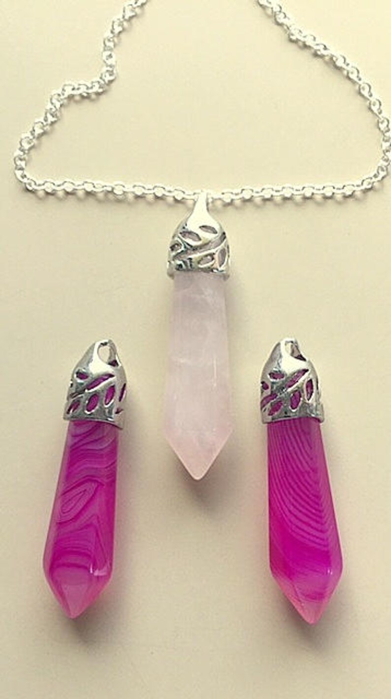 May include: Three crystal pendants on silver chains. The pendants are in the shape of a teardrop and are made of pink and white quartz.
