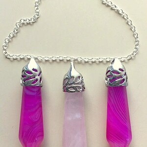 May include: A silver chain necklace with three crystal pendants. The pendants are in the shape of a point and are made of pink and white agate. The pendants are numbered 1, 2, and 3.