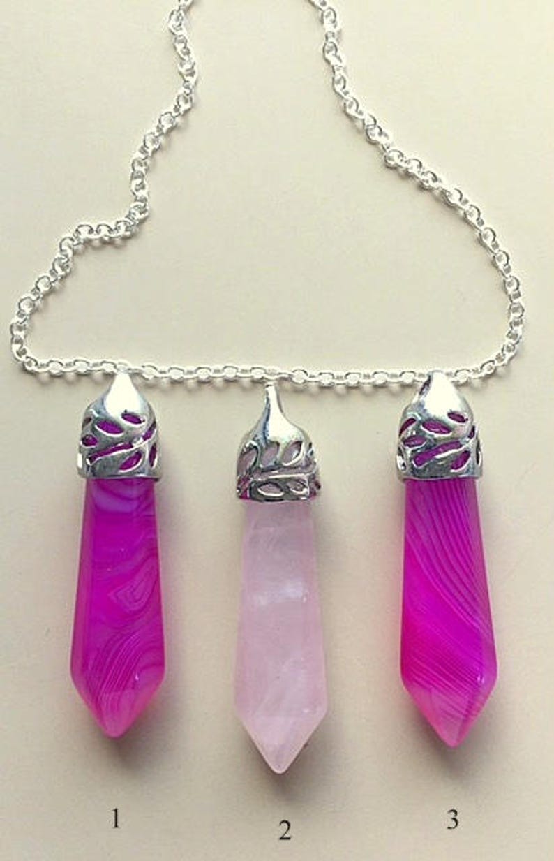 May include: A silver chain necklace with three crystal pendants. The pendants are in the shape of a point and are made of pink and white agate. The pendants are numbered 1, 2, and 3.