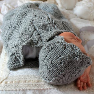 May include: A gray knitted baby hat and matching hooded sweater with a cable knit pattern.