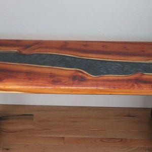 May include: A wooden bench with a black metal frame. The top of the bench is made of wood with a dark blue resin river running through it.