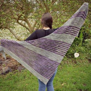 May include: A gray and purple striped shawl with a geometric pattern. The shawl is draped over a person's shoulders.