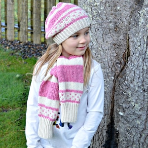 May include: A pink and white striped knitted hat and matching scarf. The hat is a slouchy beanie style with a pom pom on top. The scarf is long and thin, with a simple knit pattern.