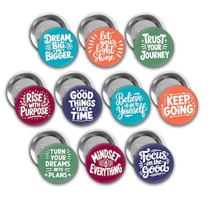 May include: A collection of round, colorful pinback buttons with motivational phrases in white script. The buttons feature phrases like "Dream Big," "Let Your Light Shine," and "Believe in Yourself." Each button has a silver metal backing.