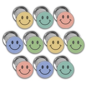 May include: Ten round, silver-colored pinback buttons with a smiley face design. The smiley faces are in various colors, including yellow, green, blue, and peach.