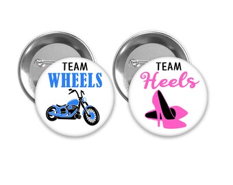 May include: Two round white button badges with silver backs. The left badge has a blue motorcycle with the text "Team Wheels". The right badge has a pink high heel shoe with the text "Team Heels".