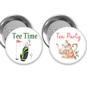 May include: Two round pinback buttons. One features a golf bag, flag, golf ball, and the words "Tee Time" in green. The other has a teapot with roses and the words "Tea Party" in pink. Both have a silver metal backing.