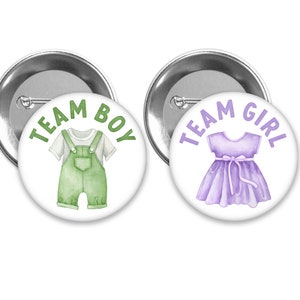 May include: Two round buttons with white backgrounds and silver borders. The left button has green text that says "Team Boy" and a green illustration of a baby in overalls. The right button has purple text that says "Team Girl" and a purple illustration of a baby in a dress.