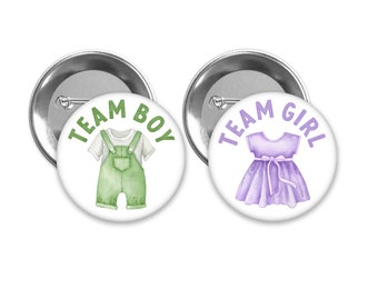 May include: Two round buttons with white backgrounds and silver borders. The left button has green text that says "Team Boy" and a green illustration of a baby in overalls. The right button has purple text that says "Team Girl" and a purple illustration of a baby in a dress.