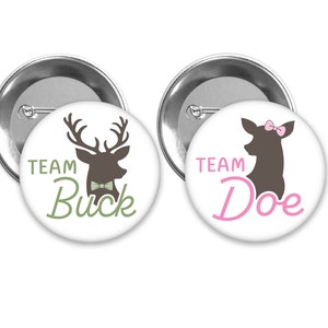 May include: Two round button pins with white backgrounds. The left pin features a brown deer silhouette with antlers and a green bow tie. The text "TEAM BUCK" is written in green below the deer. The right pin features a brown deer silhouette with a pink bow. The text "TEAM DOE" is written in pink below the deer.