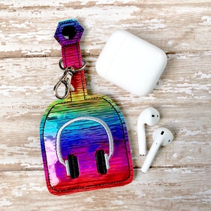 May include: A rainbow iridescent keychain with a headphone design and a silver metal clasp. The keychain is attached to a white AirPod case and two white AirPod earbuds.