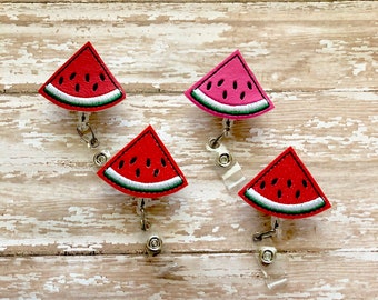May include: Four watermelon slice badge reels. Each reel features a red watermelon slice with black seeds, a green rind, and a white border. The reels are attached to a retractable cord and a metal clip.