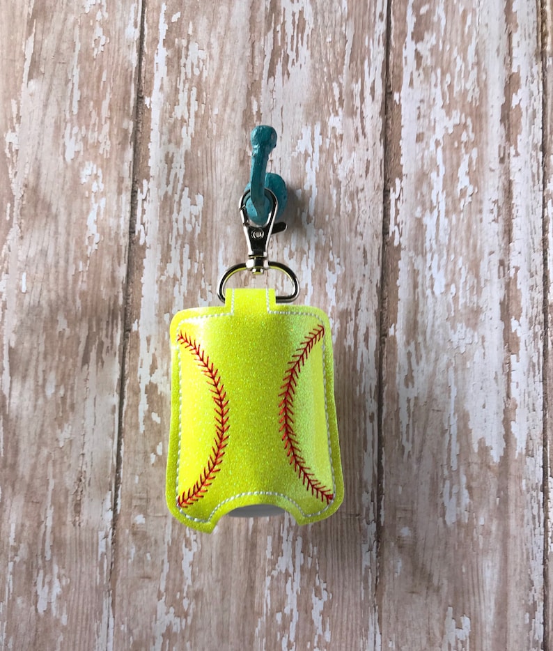 May include: A yellow and red softball-shaped hand sanitiser holder with a silver keychain.