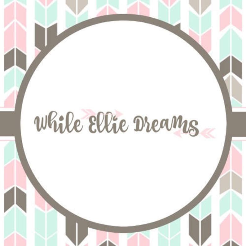 May include: A white circle with the text "while ellie dreams" in brown cursive lettering. The circle is surrounded by a pattern of pink and green arrows on a white background.
