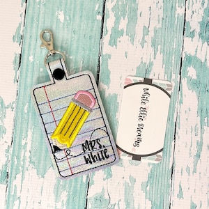 May include: A silver glitter keychain with a yellow pencil and the text "Mrs. White" on a white background. The keychain has a silver metal clasp.