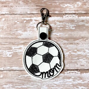 May include: White leather keychain with a black embroidered soccer ball and the word "mom" underneath.