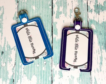 May include: Two blue and purple keychains with a clear plastic window for a card. The keychains have the text "while ellie dreams" on them.