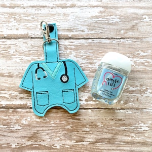 May include: A blue scrub top keychain with a stethoscope and a small bottle of hand sanitizer that says "nurse life" on it.