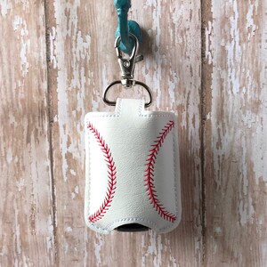 May include: White leather hand sanitiser holder with a red baseball stitch design. The holder is attached to a silver key chain and hangs from a turquoise hook.