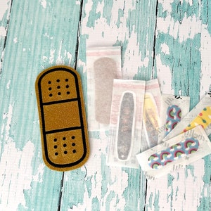 May include: A gold glitter plaster with a black outline, surrounded by several adhesive plasters with various colourful patterns, including rainbows and polka dots.