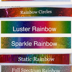 May include: A collage of seven different rainbow-colored adhesive tapes. The tapes have different textures, including scales, circles, glitter, and a static effect. The text on the tapes reads: "Rainbow Scales", "Rainbow Circles", "Luster Rainbow", "Sparkle Rainbow", "Static Rainbow", "Full Spectrum Rainbow", and "Pastel Rainbow Glitter".
