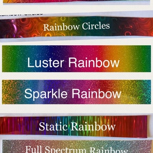 May include: A collection of seven different rainbow holographic vinyl sheets. The sheets are labeled "Rainbow Scales", "Rainbow Circles", "Luster Rainbow", "Sparkle Rainbow", "Static Rainbow", "Full Spectrum Rainbow", and "Pastel Rainbow Glitter".