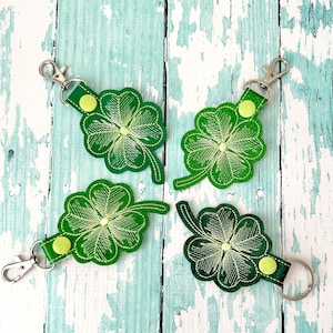 May include: Four green four-leaf clover keychains with a silver key ring. Each keychain has a green shamrock with a light green center and a silver key ring.