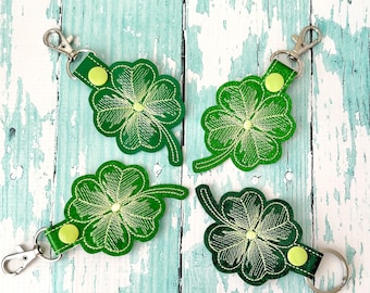 May include: Four green four-leaf clover keychains with a silver key ring. Each keychain has a green shamrock with a light green center and a silver key ring.