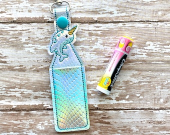 May include: A white and blue narwhal keychain with a silver iridescent lip balm holder. The lip balm is pink and yellow with the text "Carmex" and "Pink Lemonade".