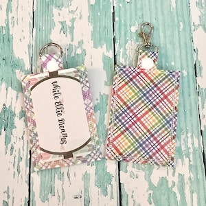 Pode incluir: Dois chaveiros com um padrão xadrez. Um chaveiro tem um fundo branco com um padrão xadrez arco-íris. O outro chaveiro tem um fundo branco com um padrão geométrico e o texto "while Ellie dreams".
