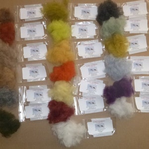 Puede incluir: Surtido de materiales de dubbing para atar moscas en varios colores, incluyendo tonos de marrón, amarillo, naranja, verde y morado. Cada color está empaquetado en una bolsa de plástico transparente con una etiqueta blanca.