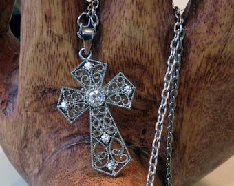 May include: A silver filigree cross pendant with clear crystal accents hangs from a silver chain.