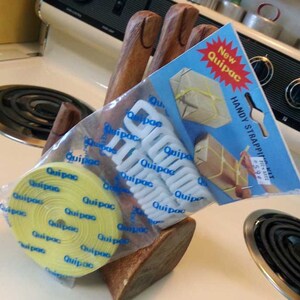 May include: A package of white plastic straps and a roll of yellow strapping tape. The package is labeled "New Quipac Handy Strapping Kit".