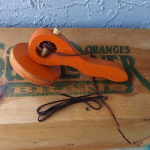 May include: Orange wooden toy with a string attached to a handle. The toy is sitting on a wooden crate with the word "ORANGES" printed on it.
