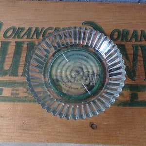May include: A clear glass ashtray with a scalloped edge. The ashtray has a small round insert with a picture of the U.S. Capitol building in Washington D.C. The insert has the text "U.S. Capitol" and "Washington D.C."