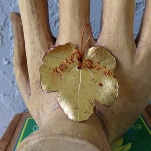 May include: A gold-colored leaf pendant with a copper wire loop and swirls. The leaf has a textured surface and is likely made of metal. The pendant is a decorative item, possibly for jewelry or crafts.