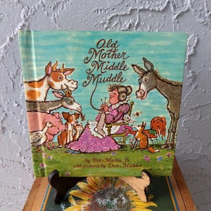 May include: A vintage children's book titled "Old Mother Middle Muiddle" by Bill Martin Jr. with pictures by Don Madden. The cover features a colorful illustration of a woman knitting with various farm animals surrounding her.
