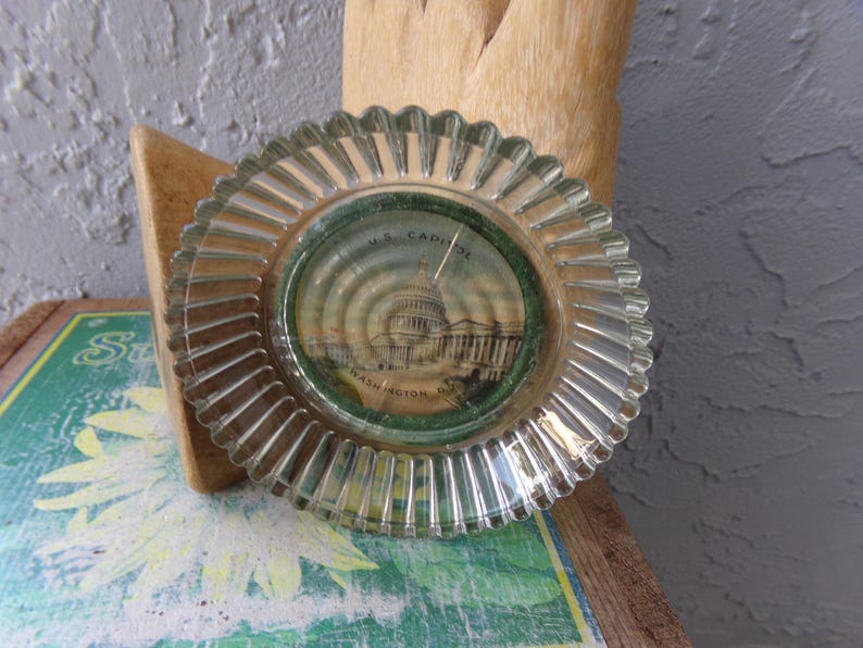 May include: A clear glass ashtray with a raised rim and a printed image of the US Capitol building in Washington, D.C.